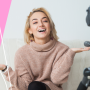 a woman sitting on a couch with a camera and a pink background